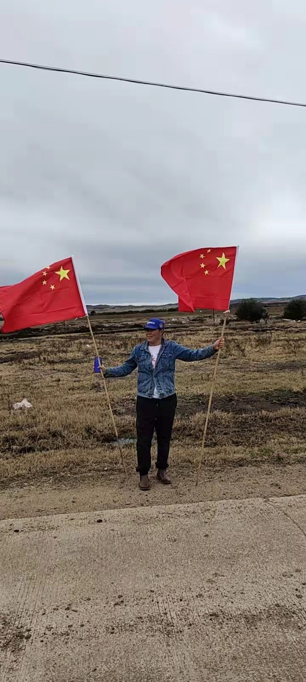 牧民手举国旗策马奔腾 身后是鹅卵石砌成的巨型国旗